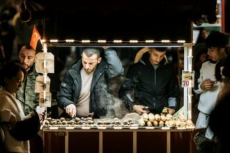 Night scene of a street vendor selling roasted chestnuts from a cart in a crowded market.